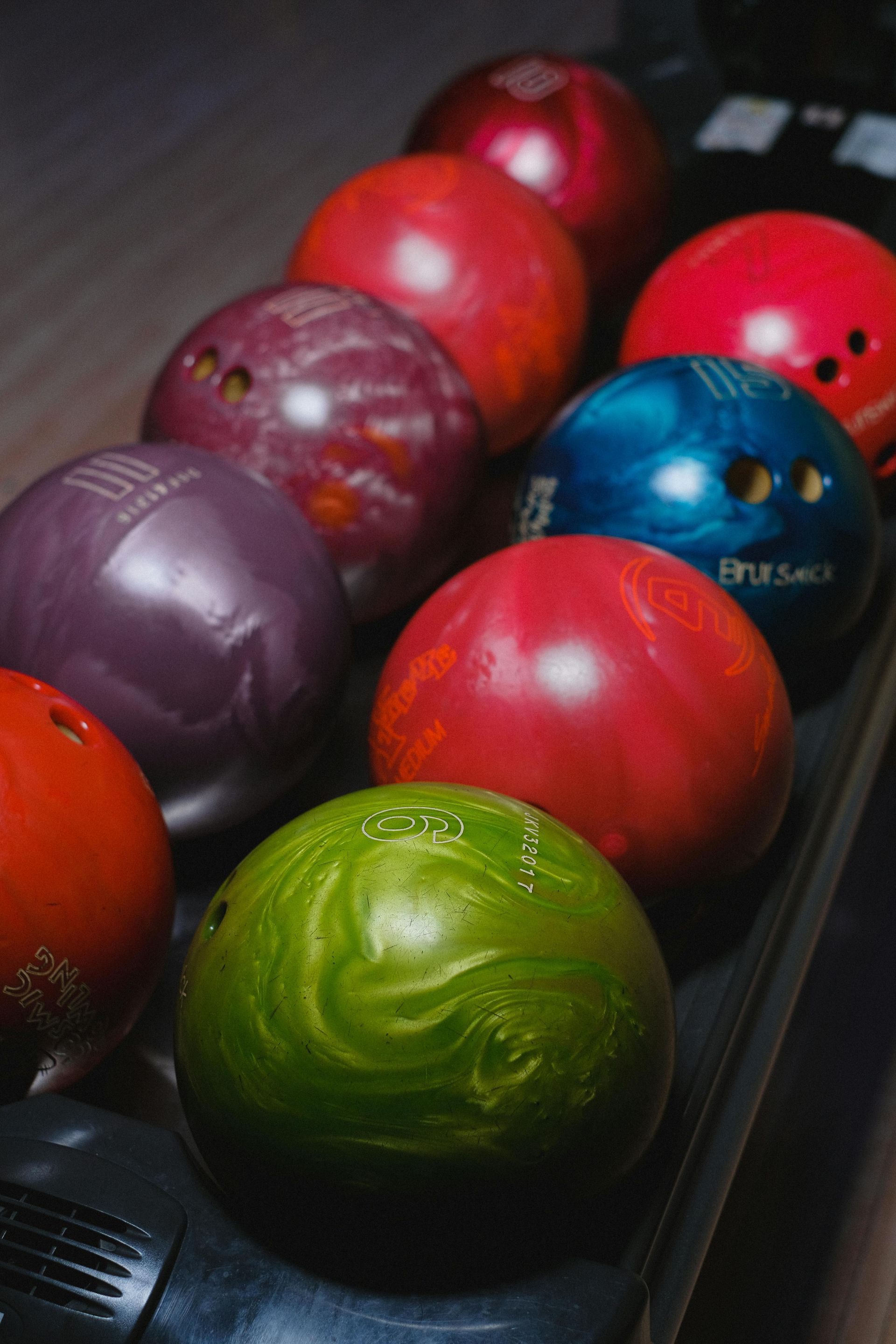 A selection of colorful bowling balls, including green, red, and purple, sitting on a ball return rack.