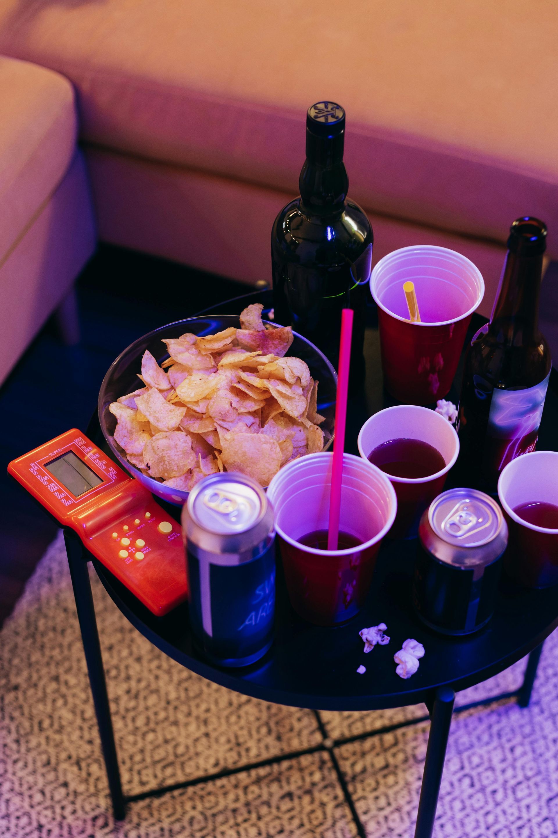 A table with potato chips, red cups, and beer bottles under purple neon lighting in a lounge area.