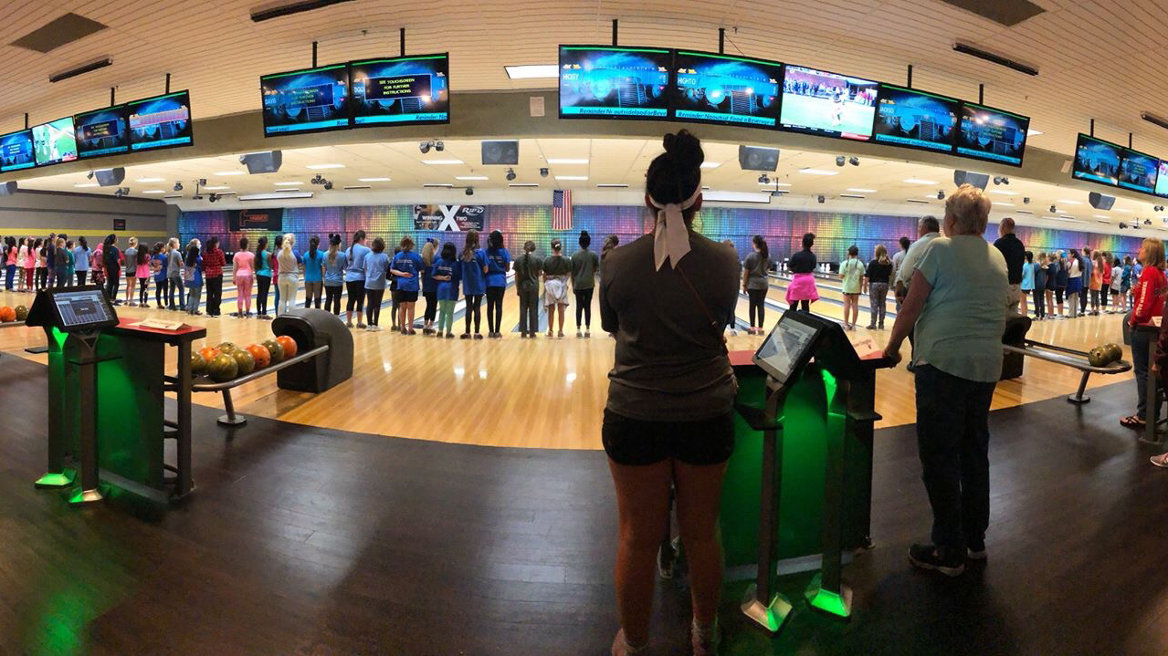 A large group of youth bowlers stands at attention across several lanes during a tournament at Plano Super Bowl.