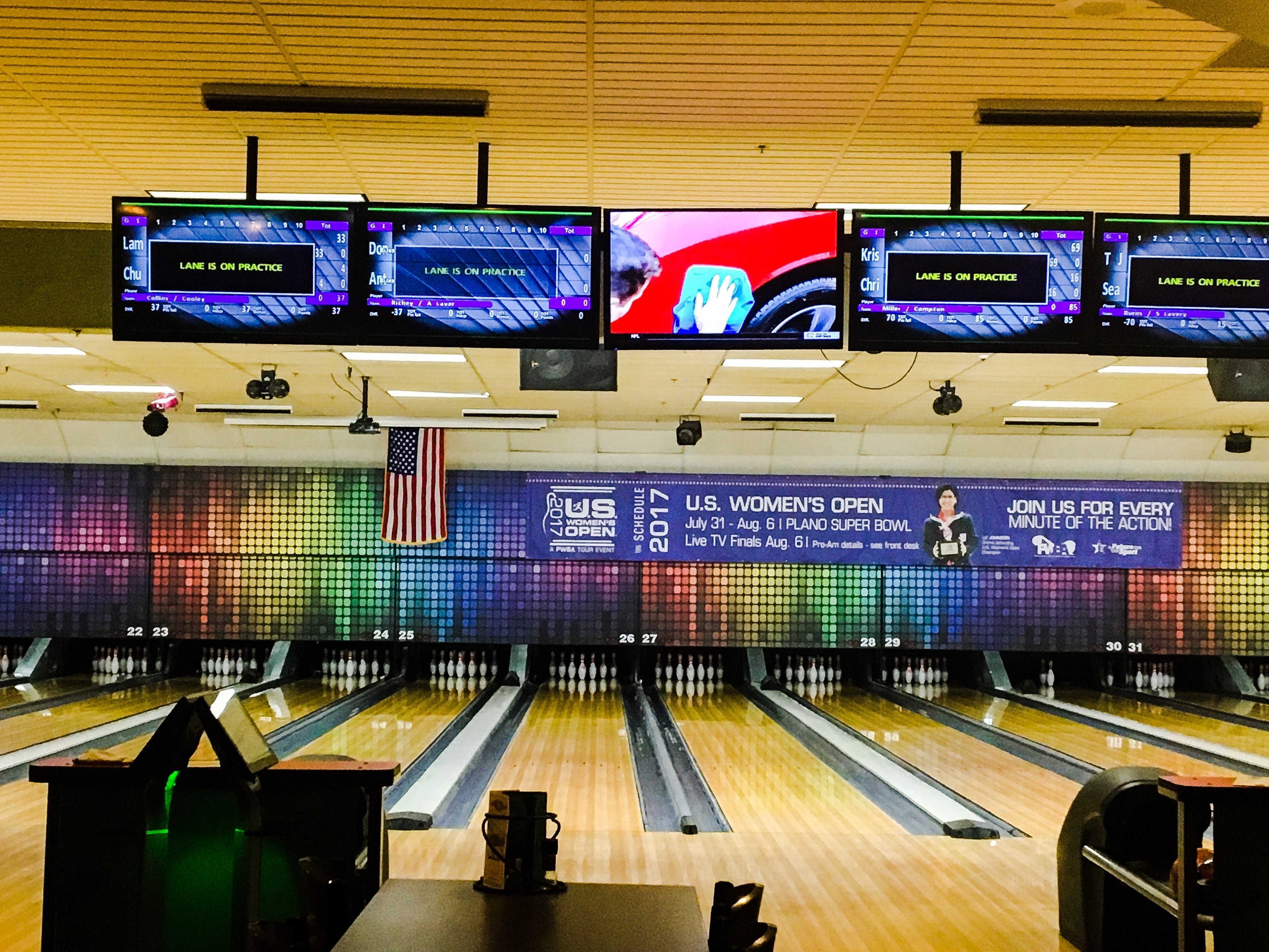 A wide view of professional bowling lanes with overhead scoring monitors and a 2017 U.S. Women's Open banner.