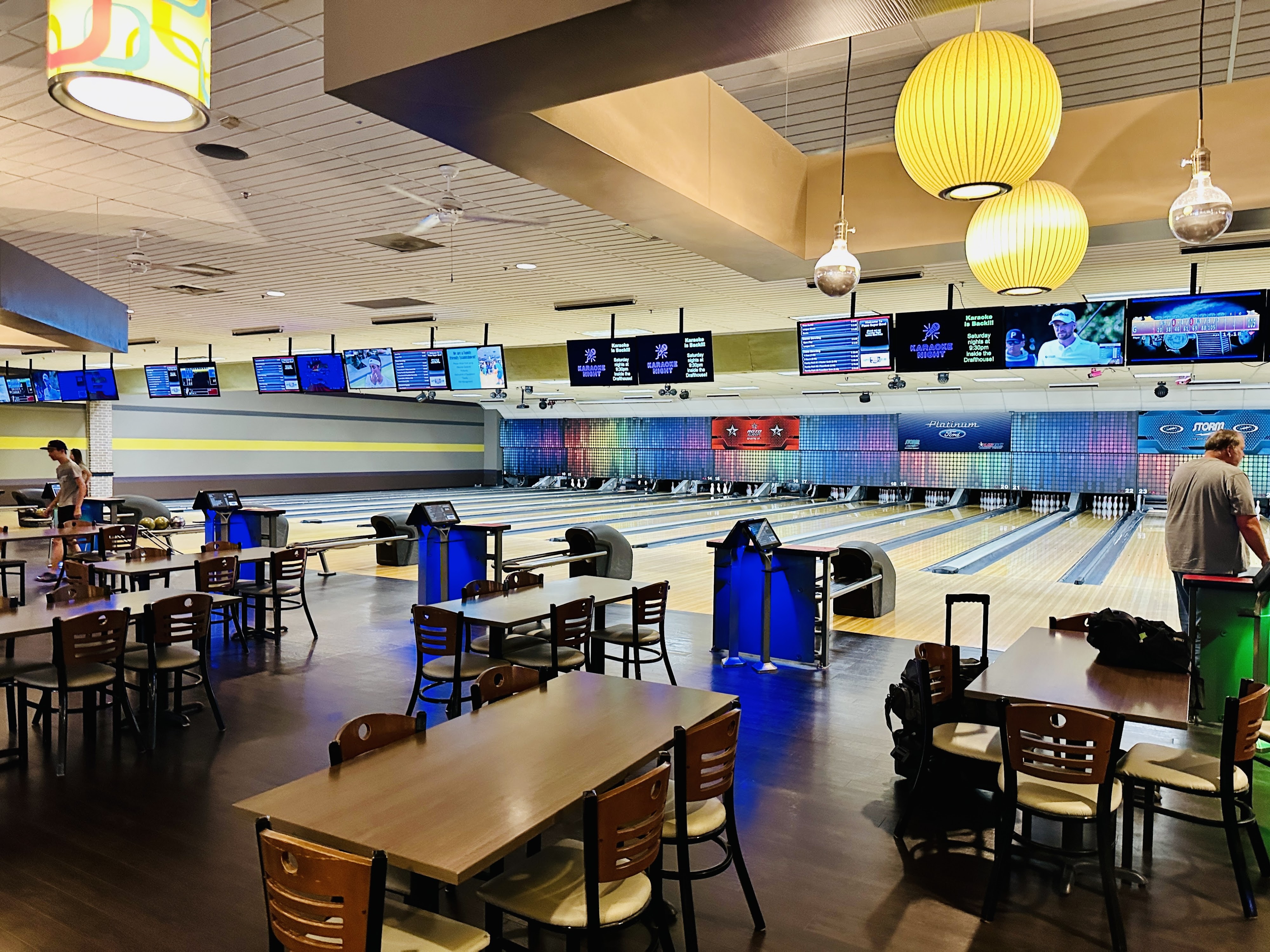A wide view of numerous bowling lanes and a seating area with wooden tables at Plano Super Bowl.