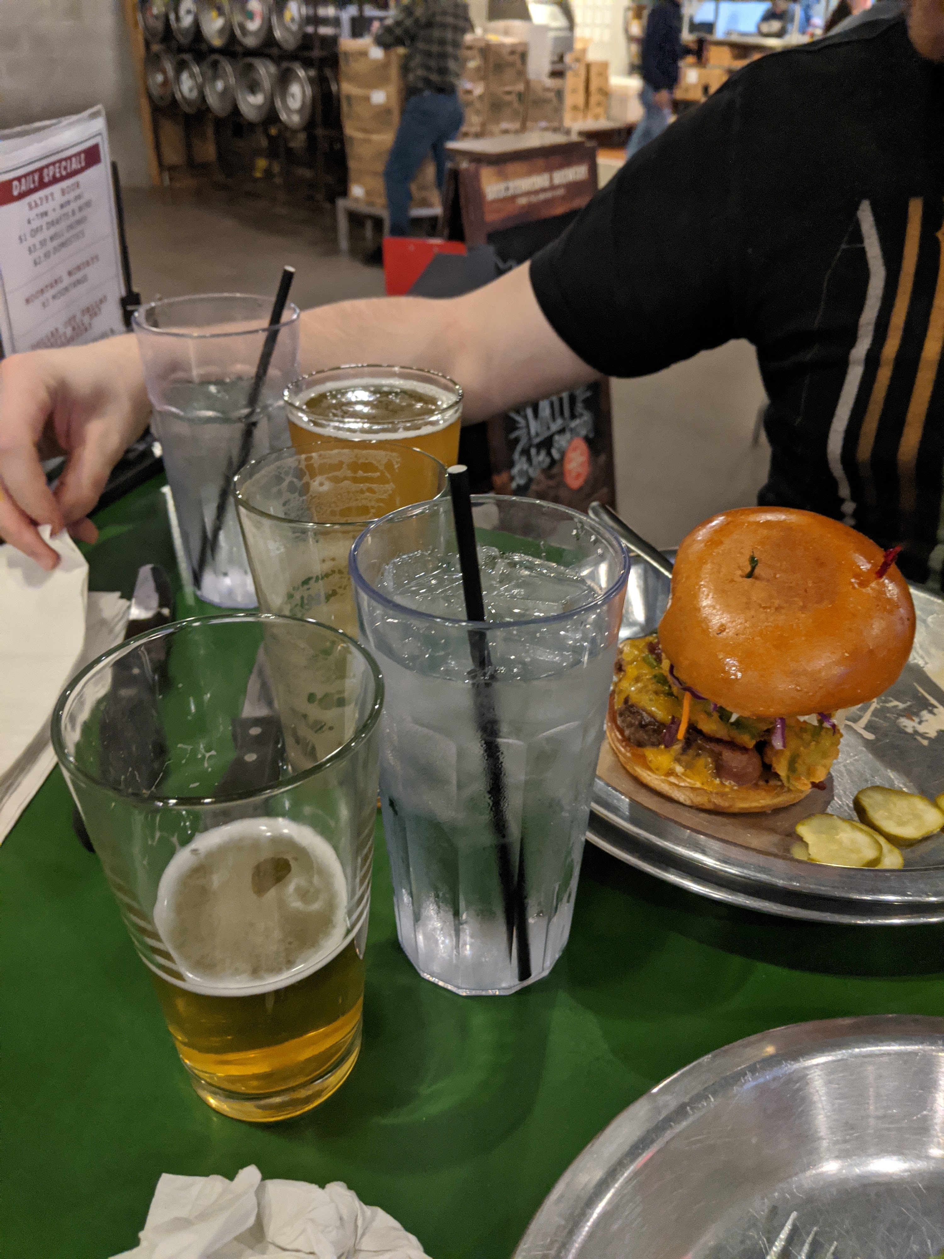 A cheeseburger and glasses of beer and water sit on a green table.