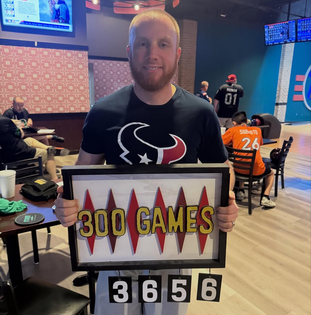A man smiling while holding a plaque that says 300 Games inside a bowling center.