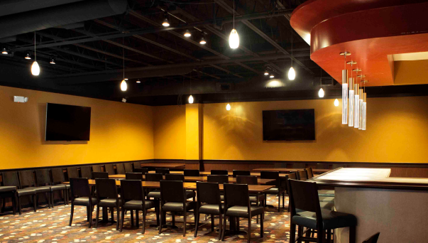 A spacious private event room with rows of tables and chairs, wall-mounted TVs, and a bar counter area.