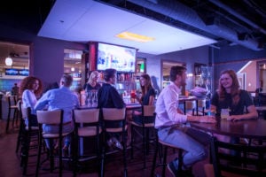 Guests sitting at a bar and lounge tables under blue ambient lighting.