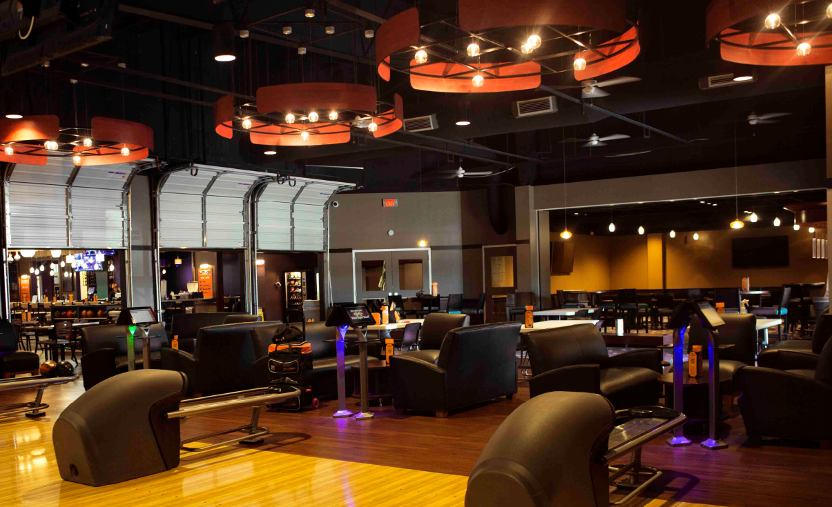 Upscale bowling alley interior with leather sofas, digital scoring tablets, and large circular chandeliers.