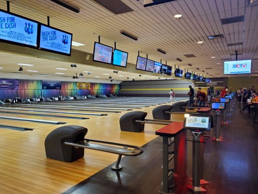 Wide interior view of multiple bowling lanes with automatic scoring monitors and tournament signage on the screens.