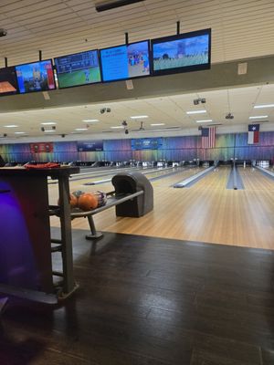 A view of multiple bowling lanes with wooden surfaces, scoring monitors, and house balls on a return rack.