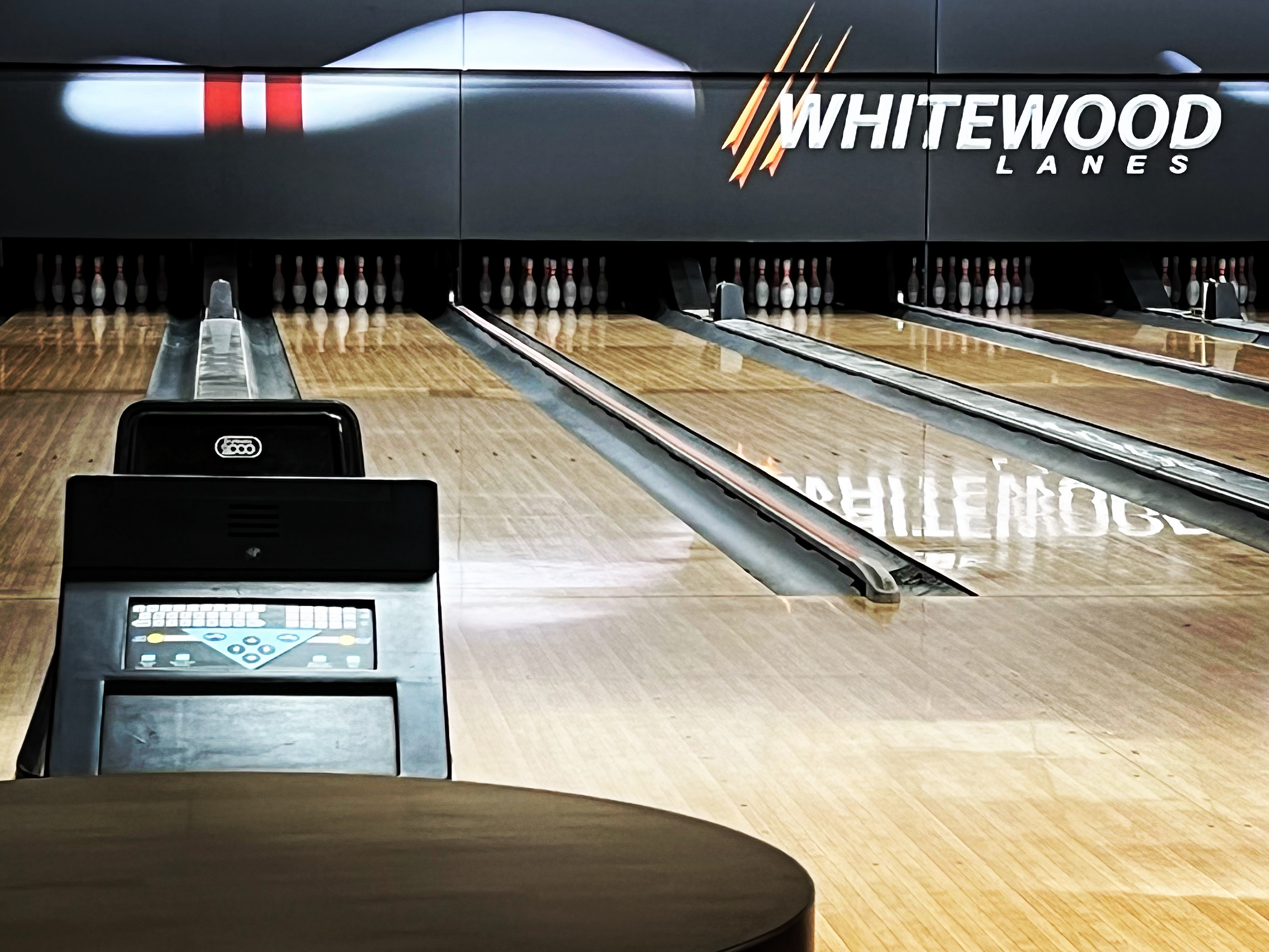 A close-up view of three bowling lanes with pins set, featuring the Whitewood Lanes logo and an automatic scoring console.