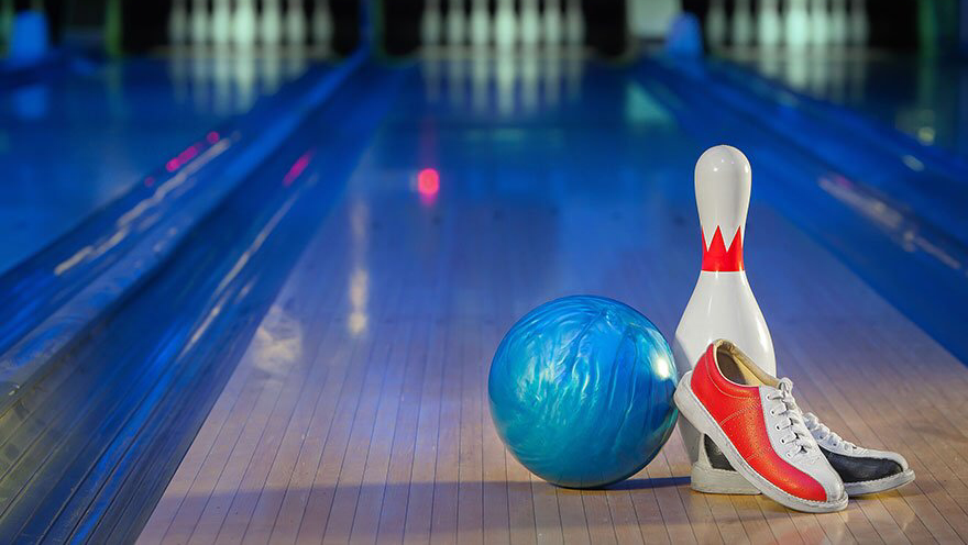 A blue bowling ball, a white bowling pin, and a pair of red and white bowling shoes sit on a bowling lane.