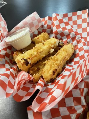 Close-up of fried food sticks with a side of dipping sauce in a red and white checkered basket.