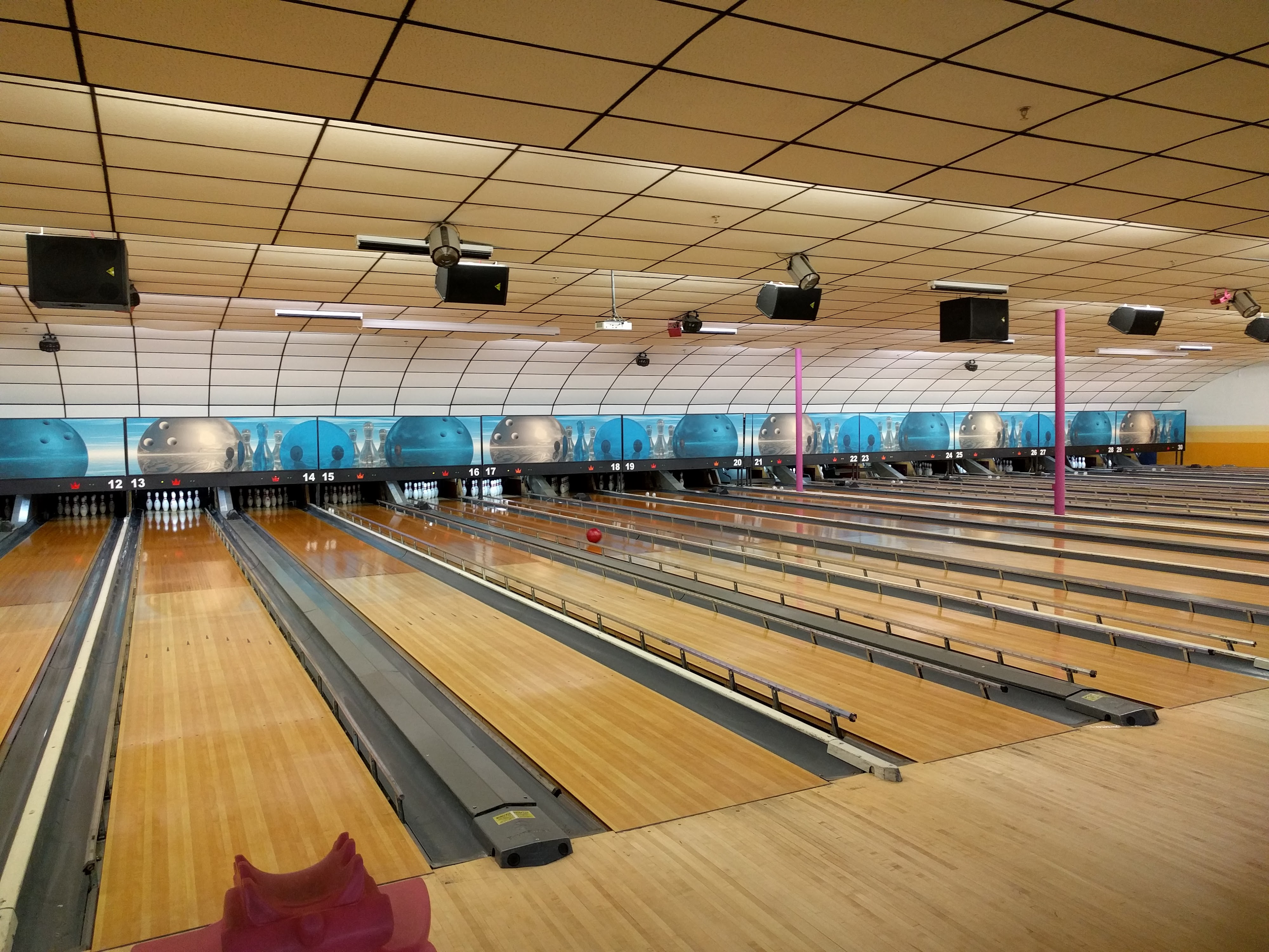 A wide-angle view of several polished wooden bowling lanes with a red ball rolling toward the pins.