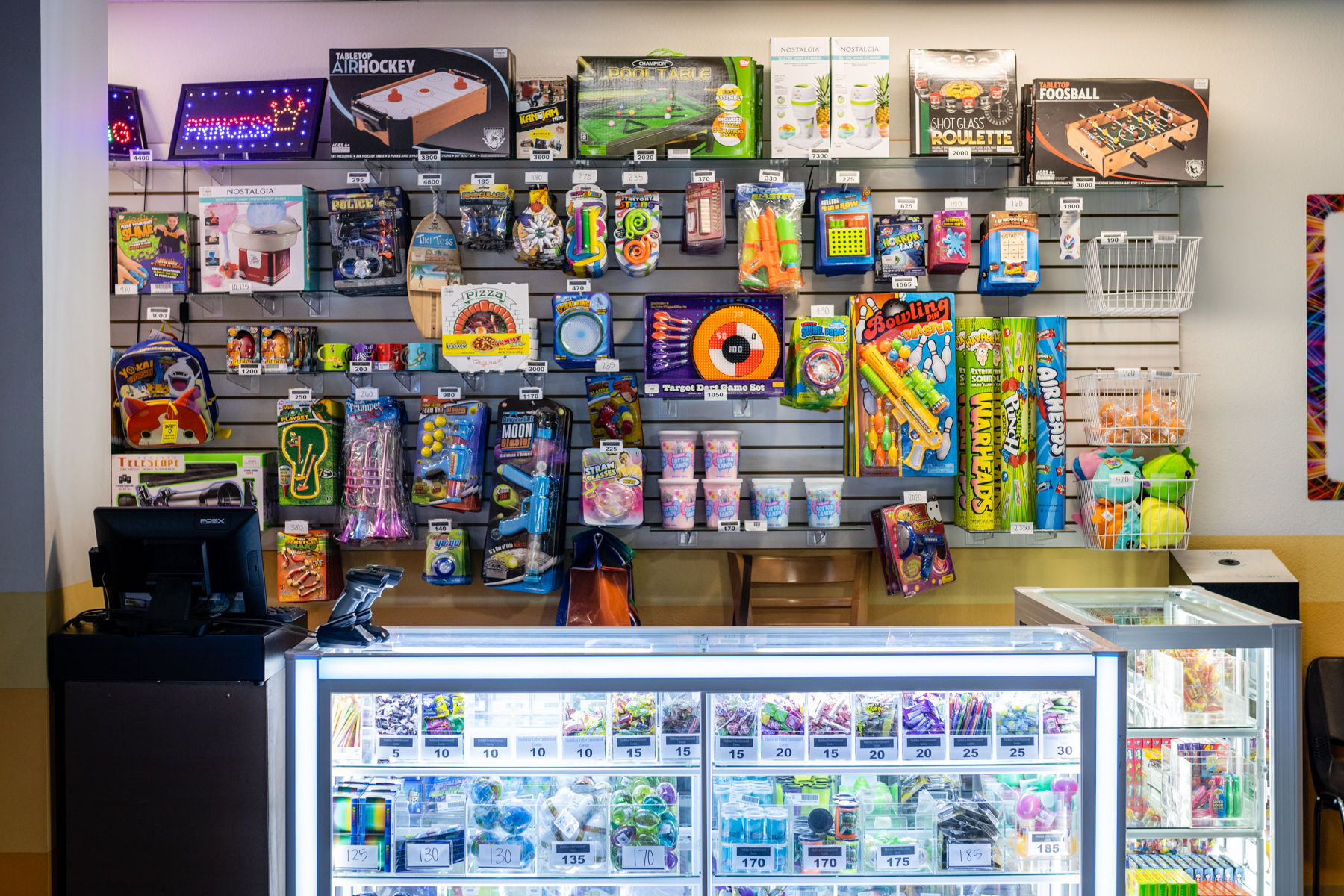 A bright arcade redemption counter with wall shelves of toys and glass cases filled with prizes and candy.