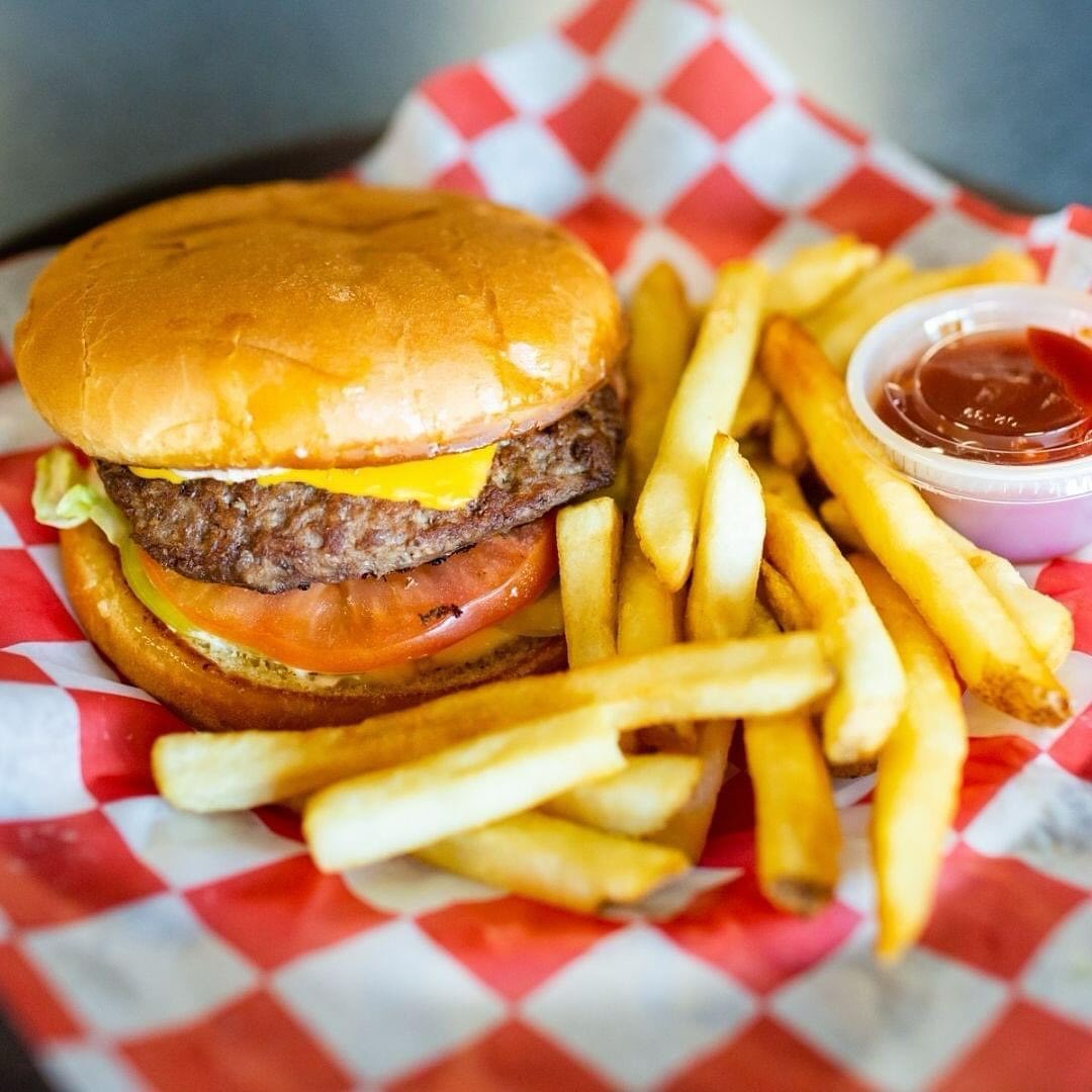 A cheeseburger with melted cheese and tomato served with a side of french fries on checkered paper.