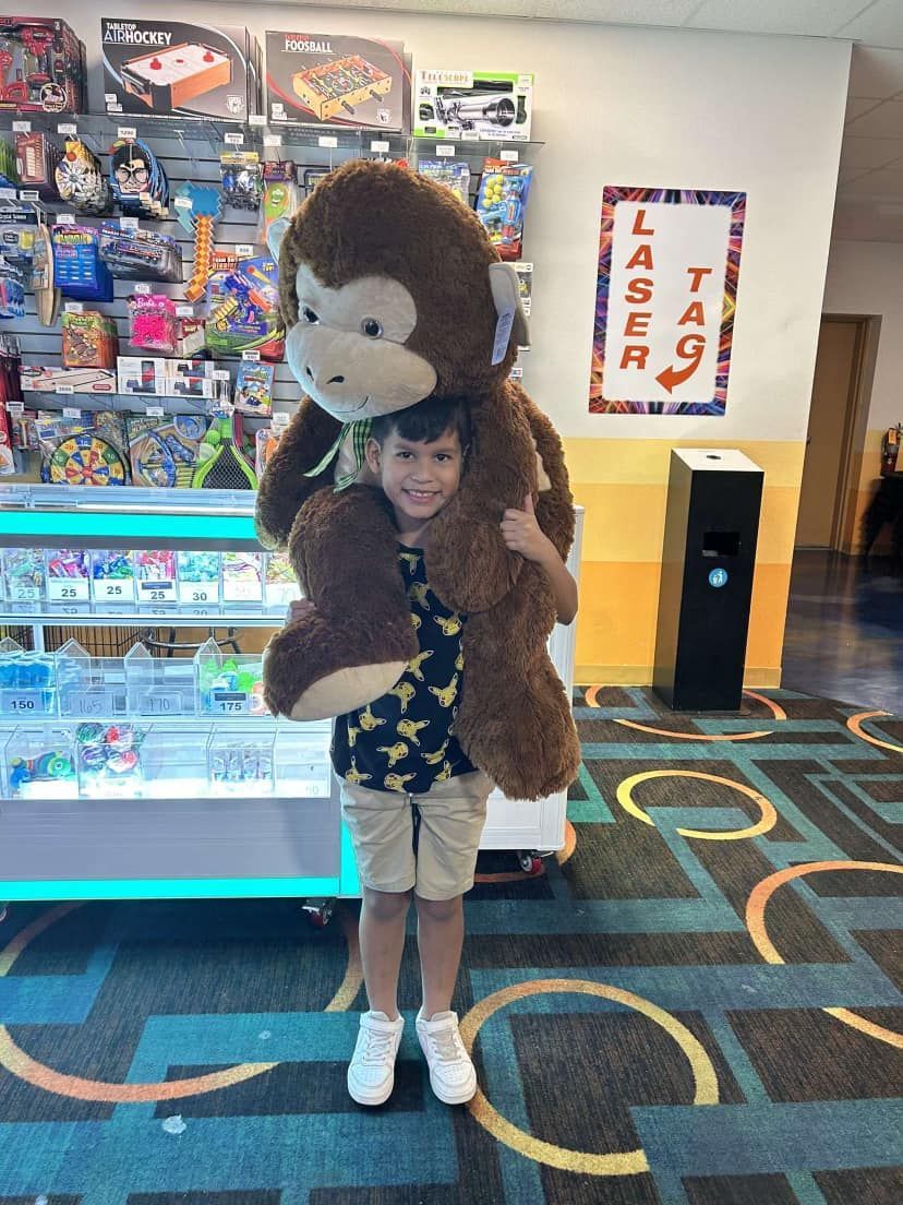 A smiling boy holding a giant stuffed monkey prize in front of an arcade redemption counter.
