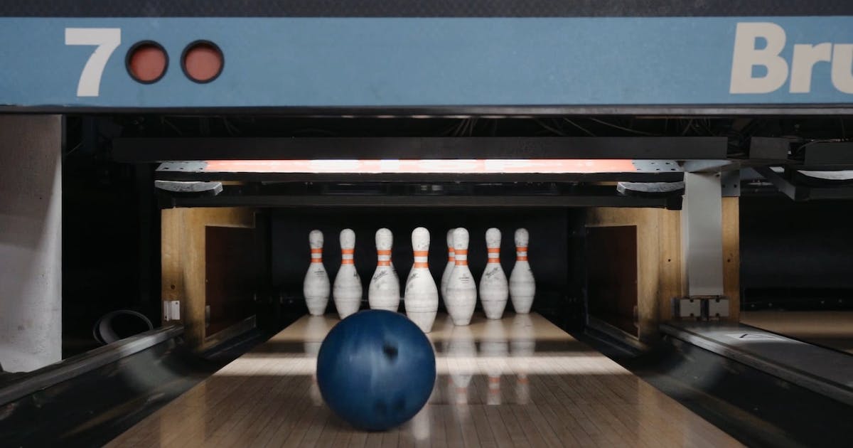 A blue bowling ball rolls down a wooden lane toward a full set of ten white pins.