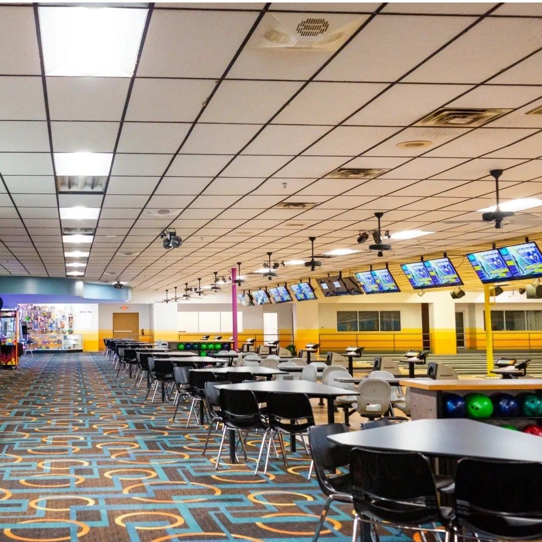 Interior of a clean bowling center with numerous tables, scoring monitors, and lane equipment.