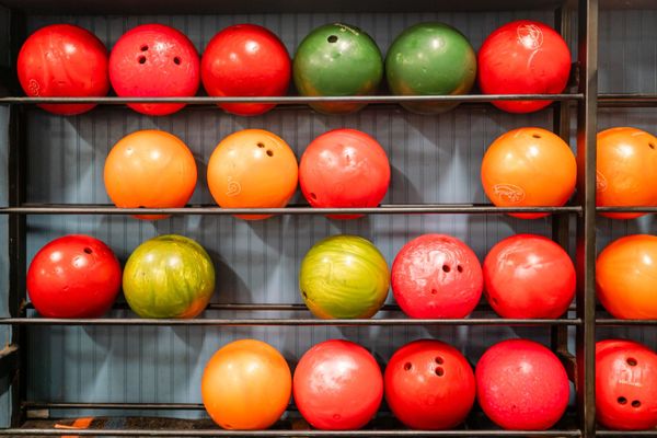 A storage rack filled with rows of colorful red, orange, and green bowling balls.