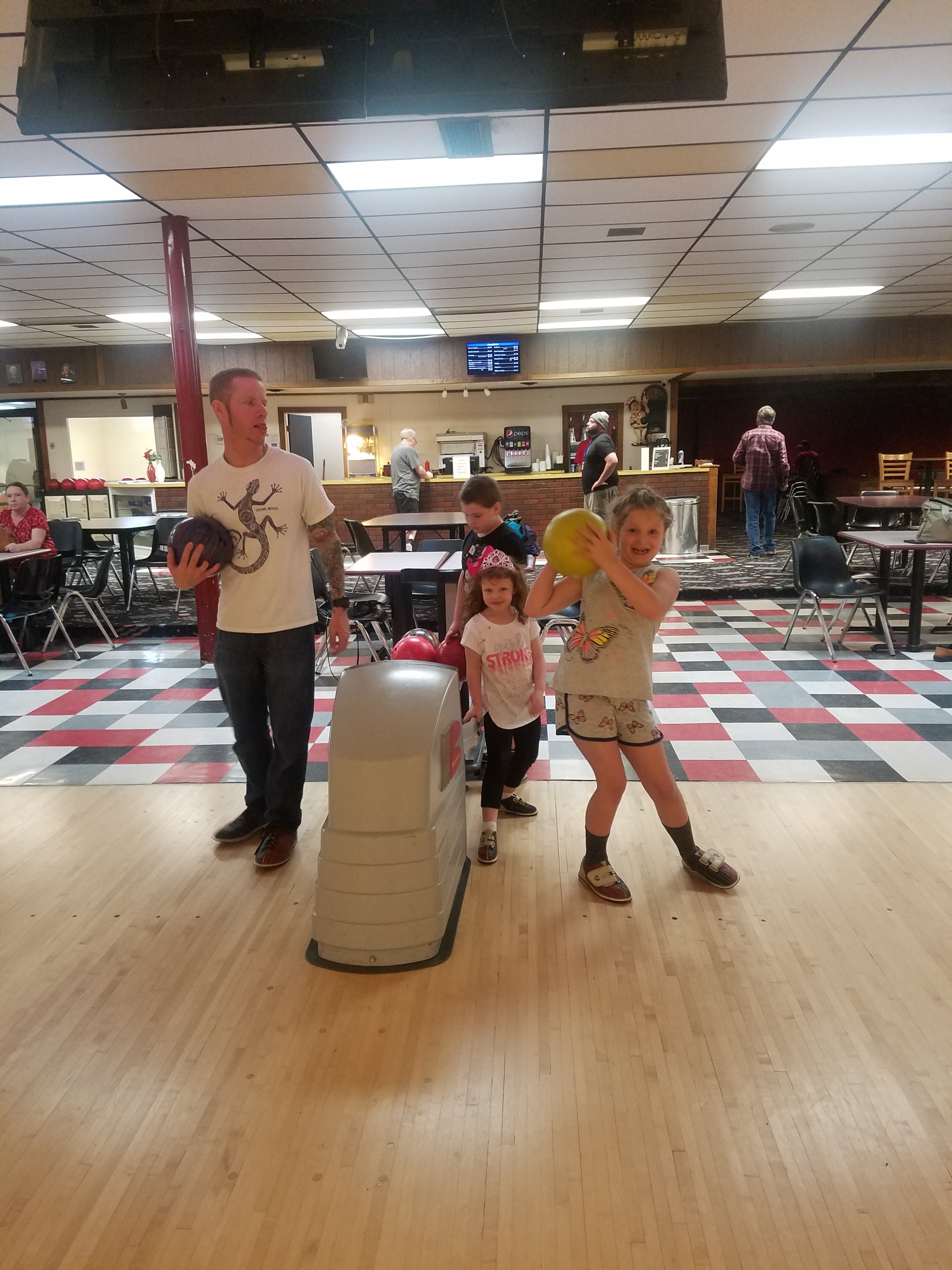 An adult and three children holding bowling balls at the start of a lane in a bowling center.