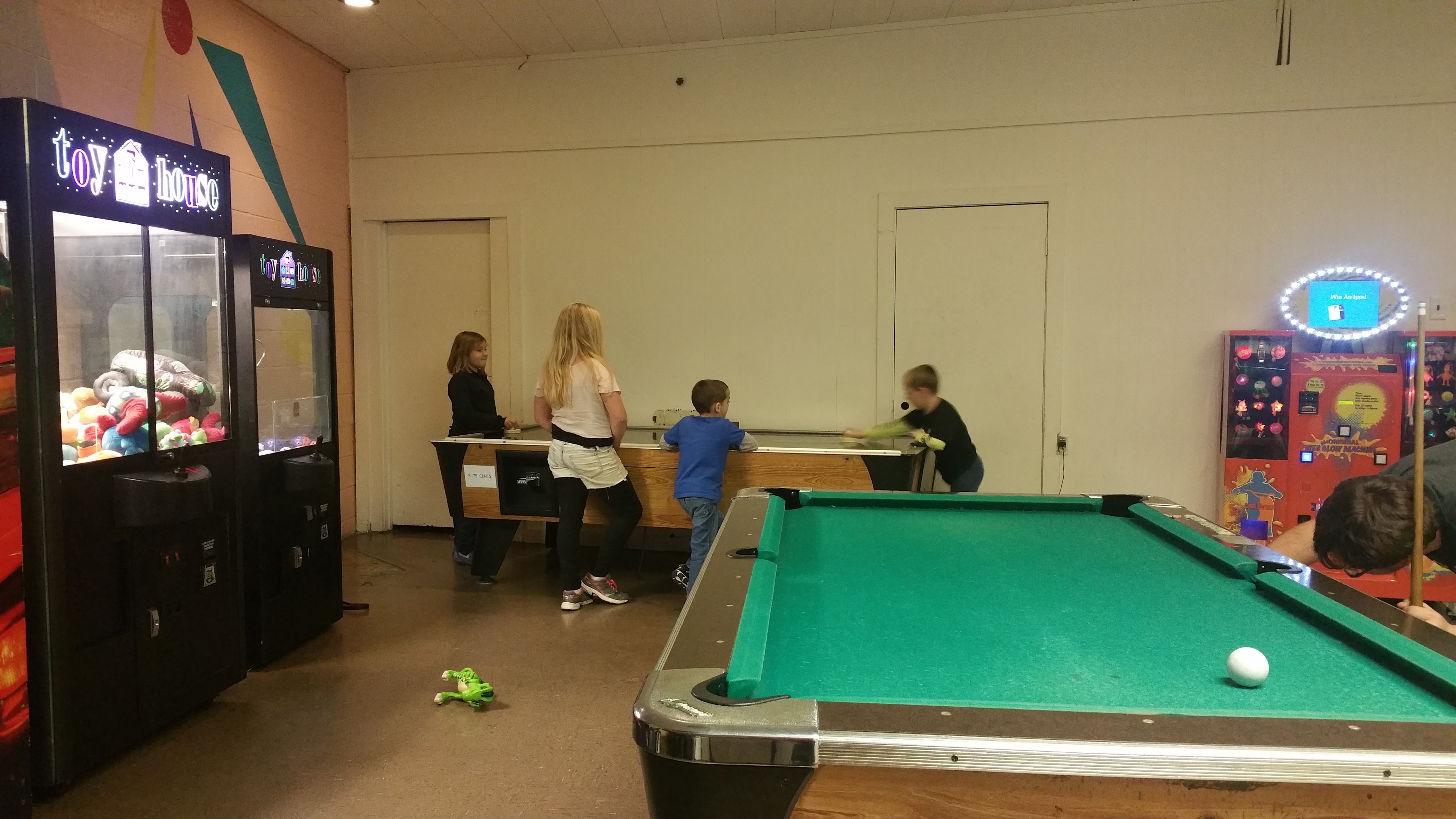 Children playing air hockey in an arcade area featuring a pool table and claw machines.