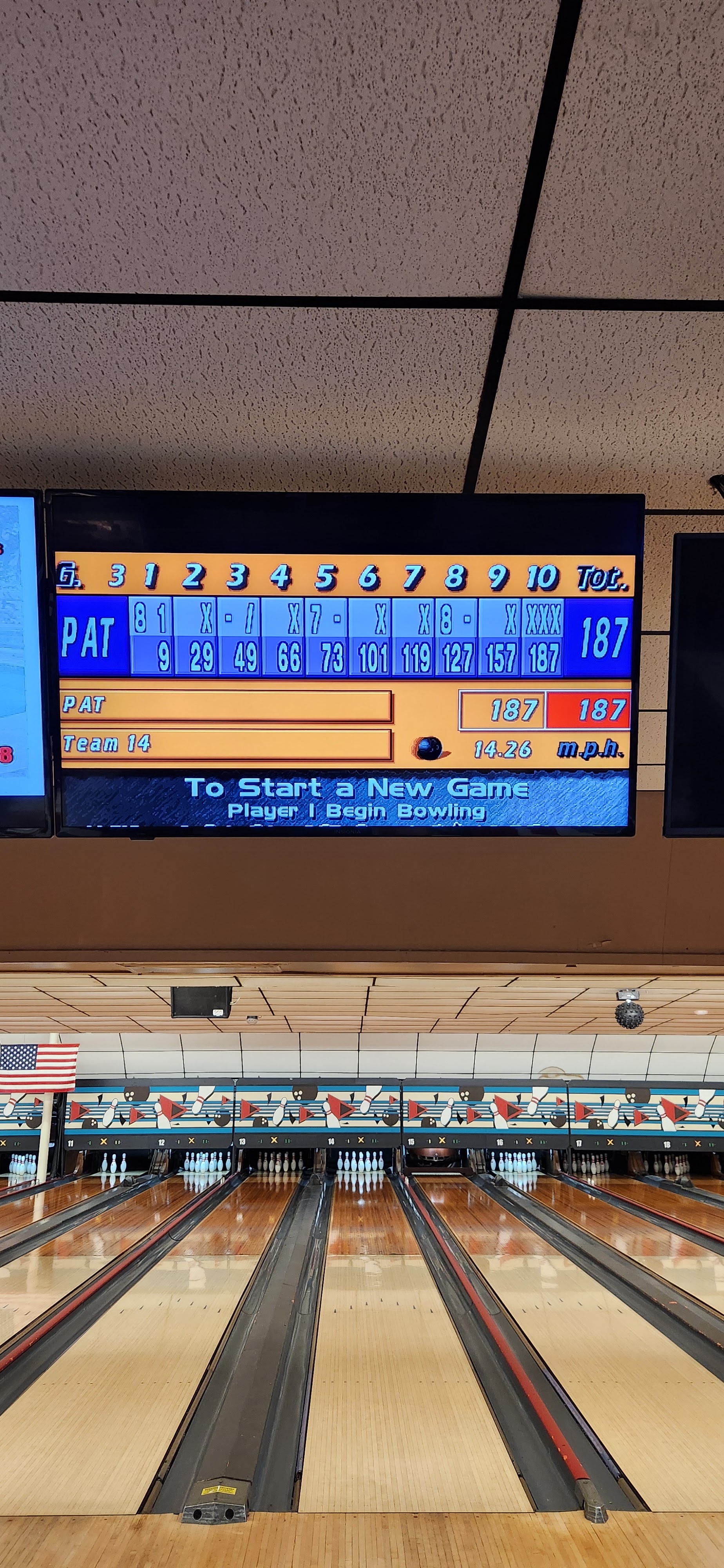 Vertical view of wooden bowling lanes and an overhead digital monitor showing a final score of 187.