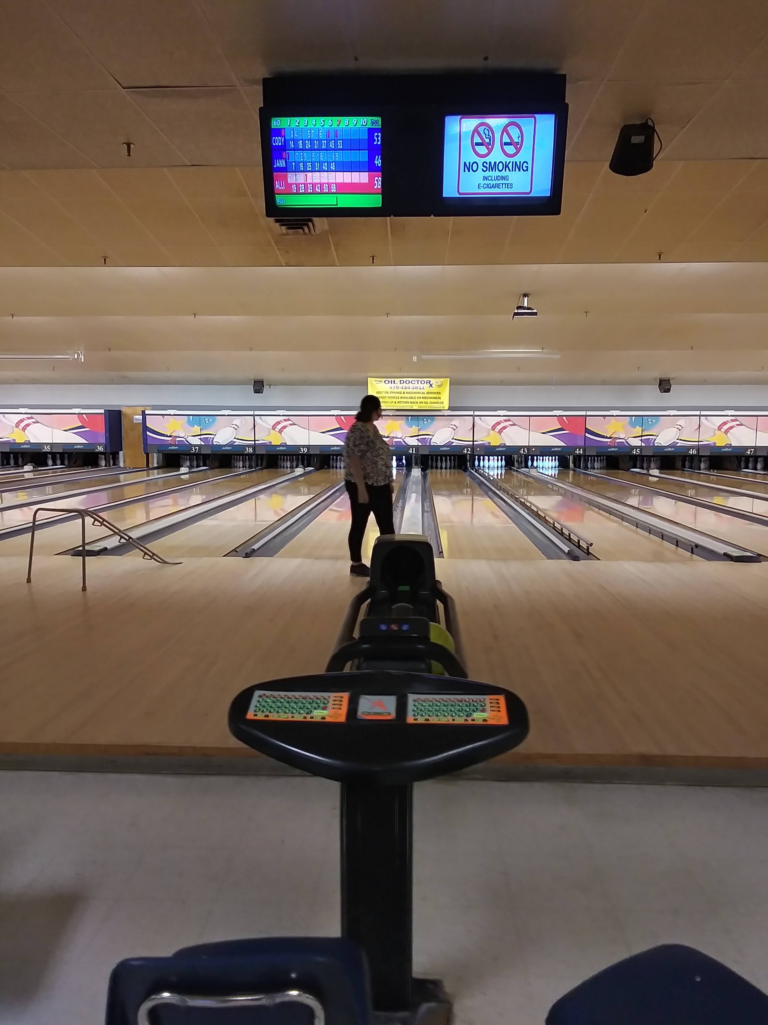 A bowler stands on a lane, preparing to bowl, with scoring screens visible above the lanes.