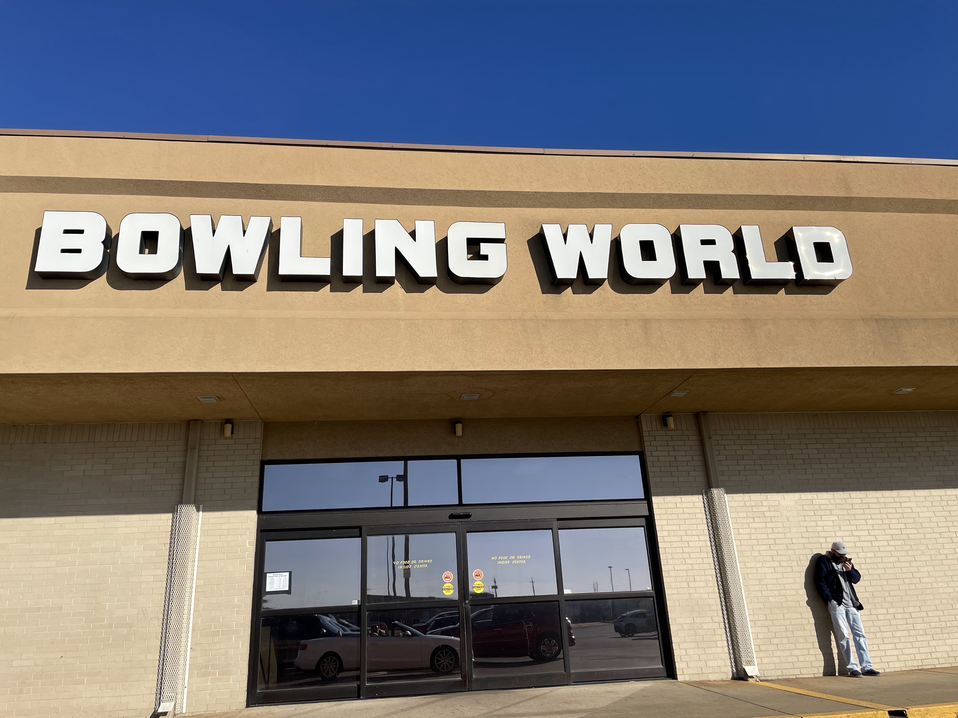 The exterior of Bowling World, featuring its prominent sign above the main entrance doors under a clear blue sky.