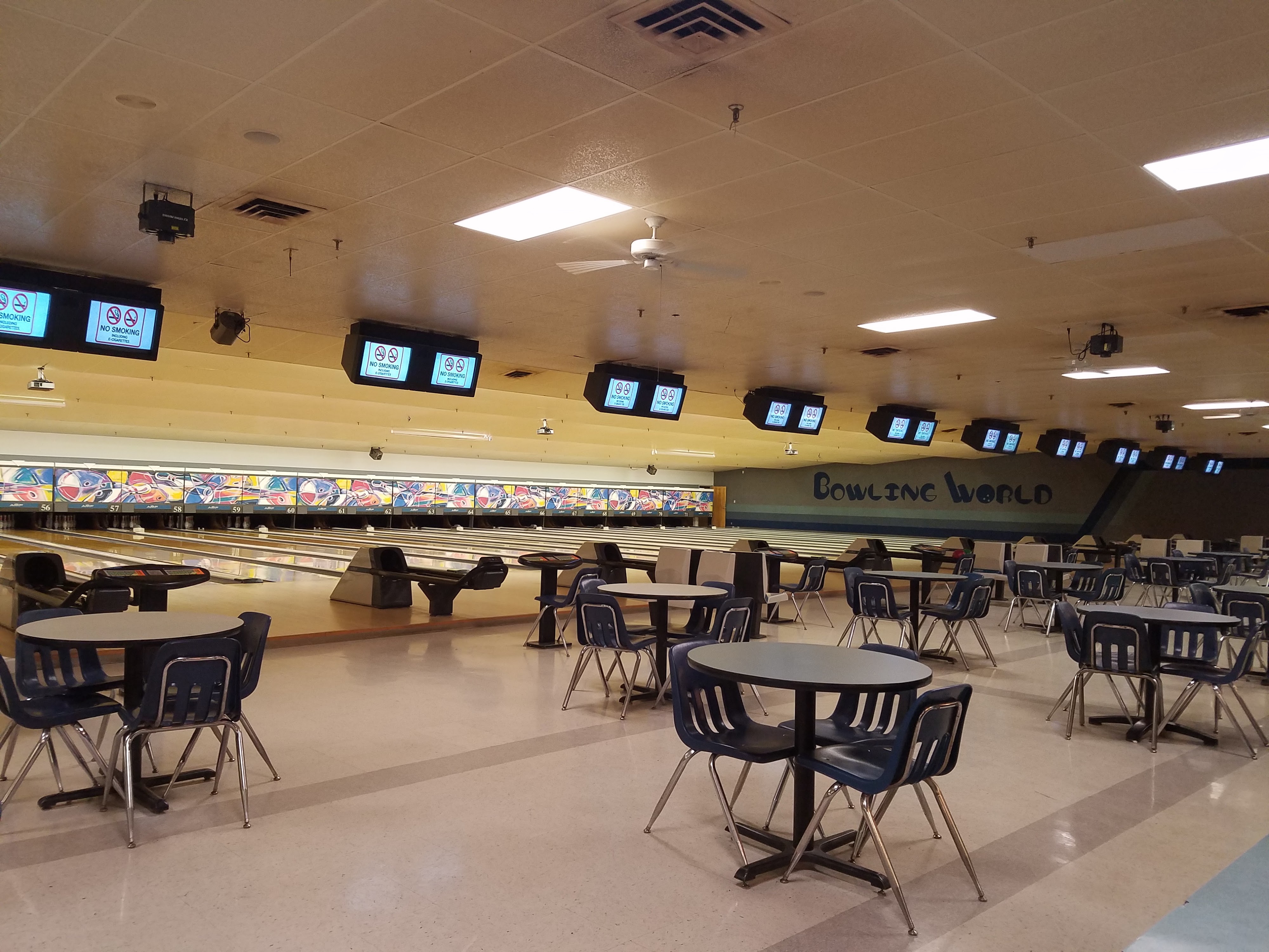 A wide interior shot of multiple brightly lit bowling lanes, each with an overhead automatic scoring screen displaying "No Smoking" signs.