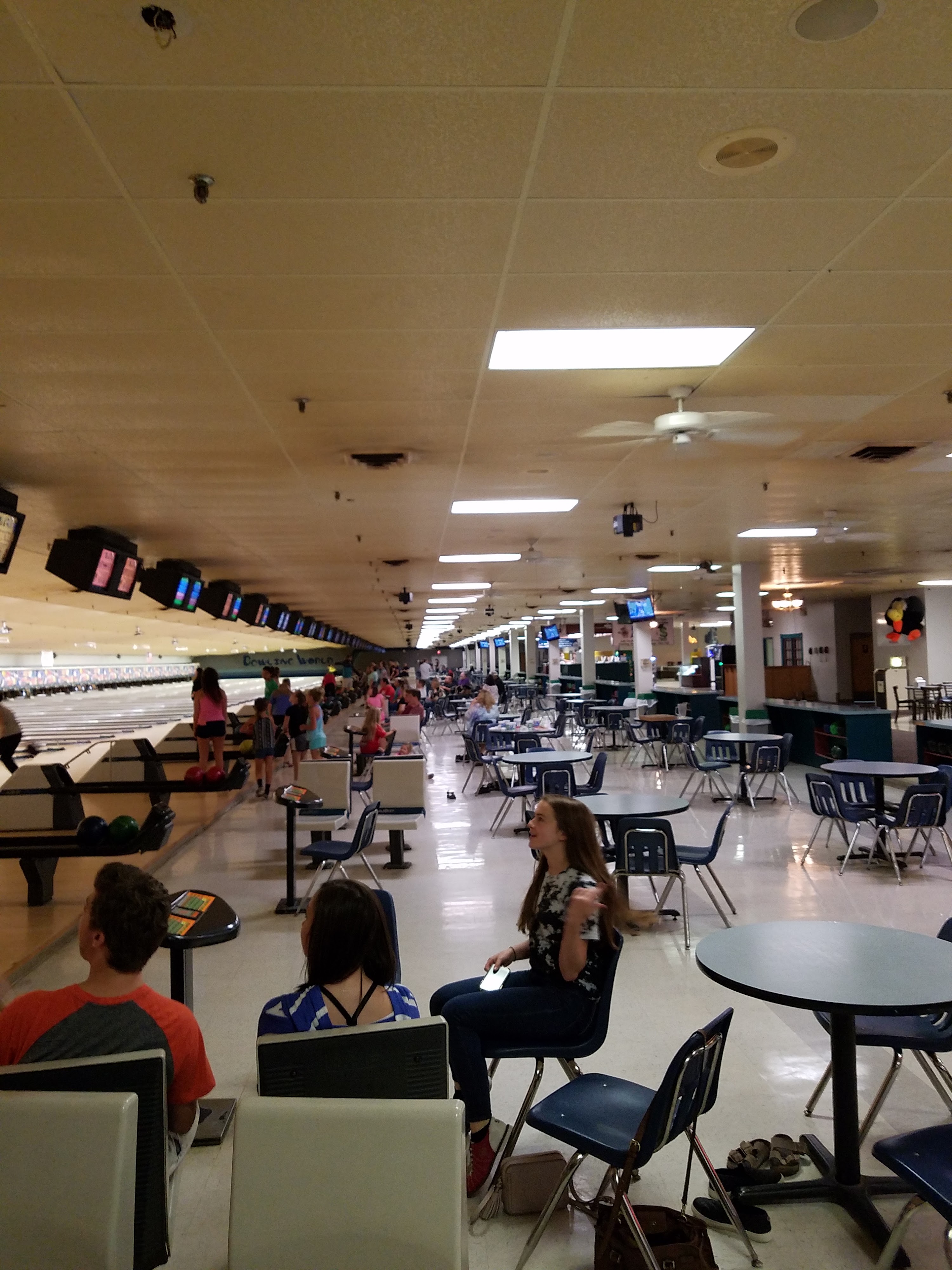 An indoor bowling alley with multiple lanes, people bowling, and seated guests at tables.