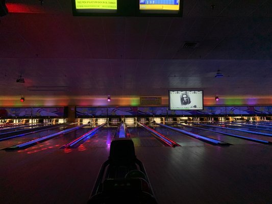 View down multiple bowling lanes illuminated with neon blue and red lights in a cosmic bowling setting.