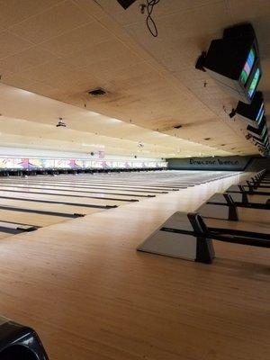 A wide, empty bowling alley features multiple lanes stretching into the distance with overhead scoring monitors.