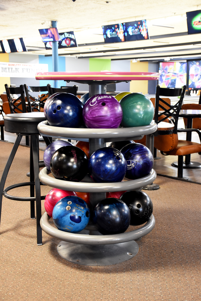 A three-tiered circular rack filled with colorful bowling balls in a bowling center concourse.