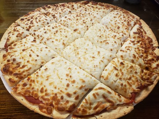A large thin-crust cheese pizza cut into square slices on a wooden table.