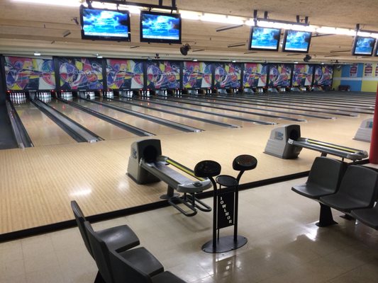 Wide interior view of several polished bowling lanes with overhead monitors and seating at Bowlmor Lanes.