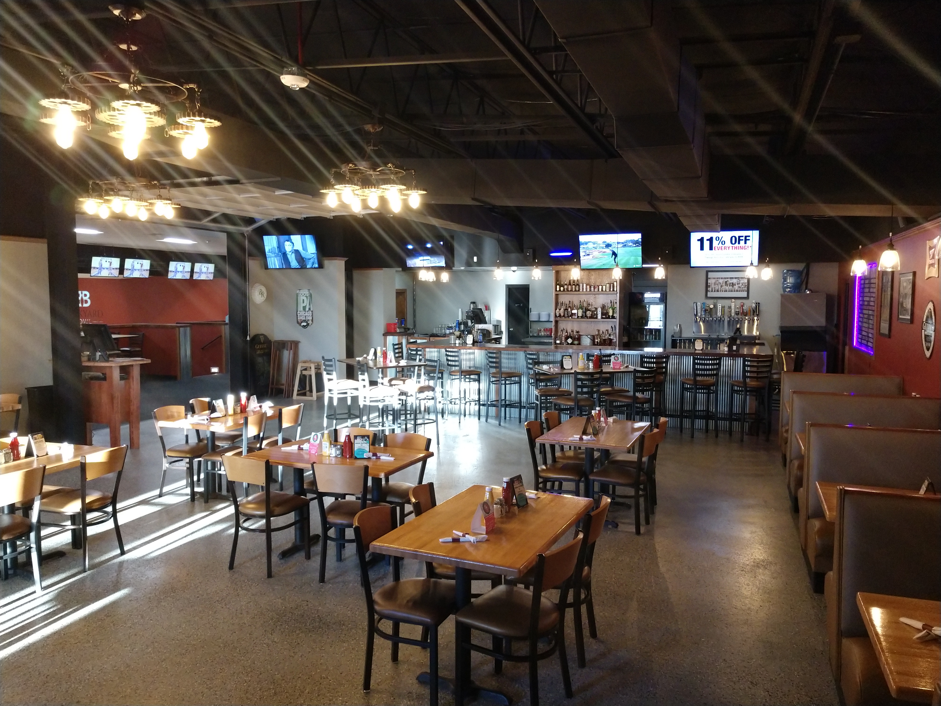 Spacious dining area and bar with wooden tables and industrial gear-shaped chandeliers.