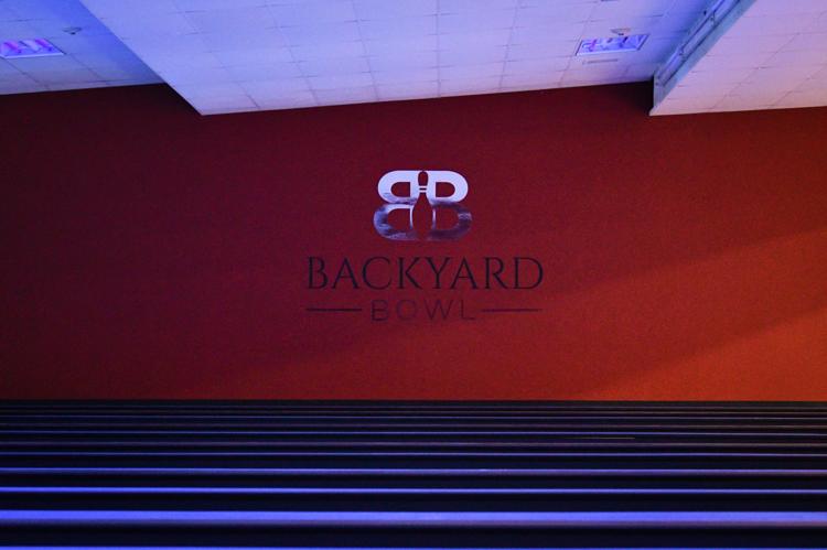 The Backyard Bowl logo on a red wall with bowling lanes in the foreground under blue lights.