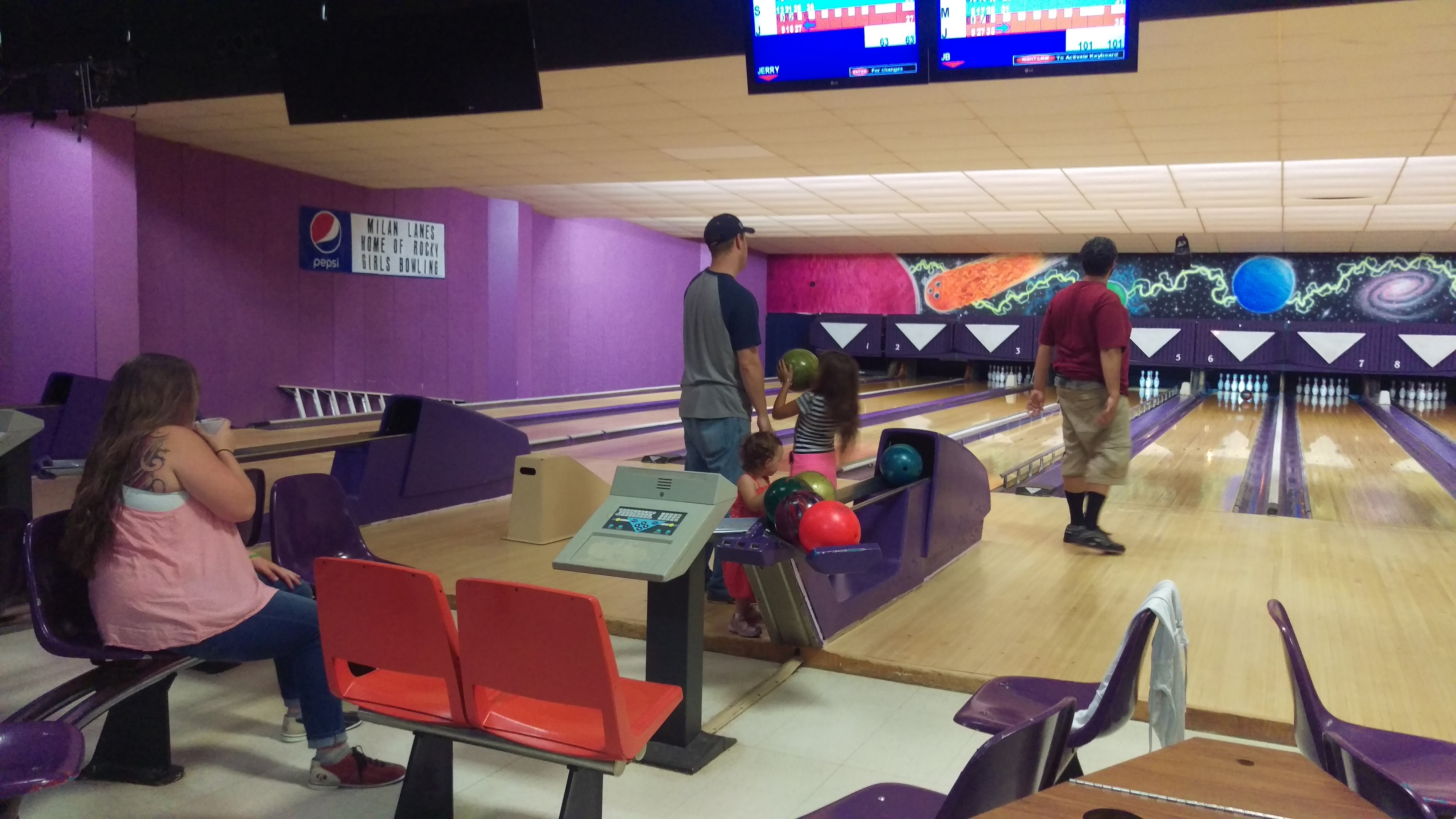 A family bowls together at a bowling center with purple walls and a space-themed mural.