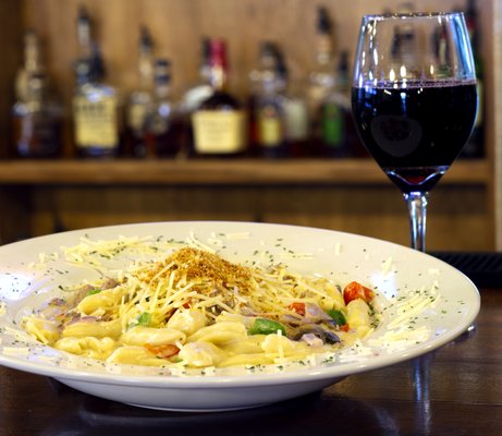A plate of creamy pasta with cheese and a glass of red wine on a bar counter.