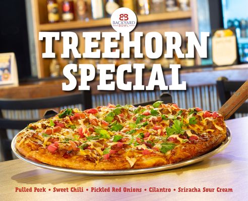 A gourmet pizza with pulled pork and cilantro on a metal tray in front of a blurred bar.