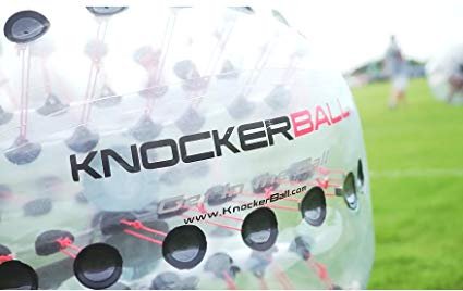 A close-up of a clear inflatable KnockerBall bubble suit on a bright green grass field.