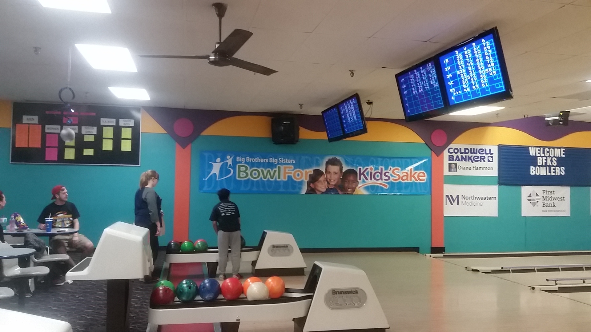 People bowling at Mardi Gras Lanes during a Bowl For Kids' Sake charity event with colorful banners in the background.