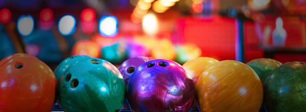 Close-up row of colorful bowling balls on a rack with blurred neon lights in the background.
