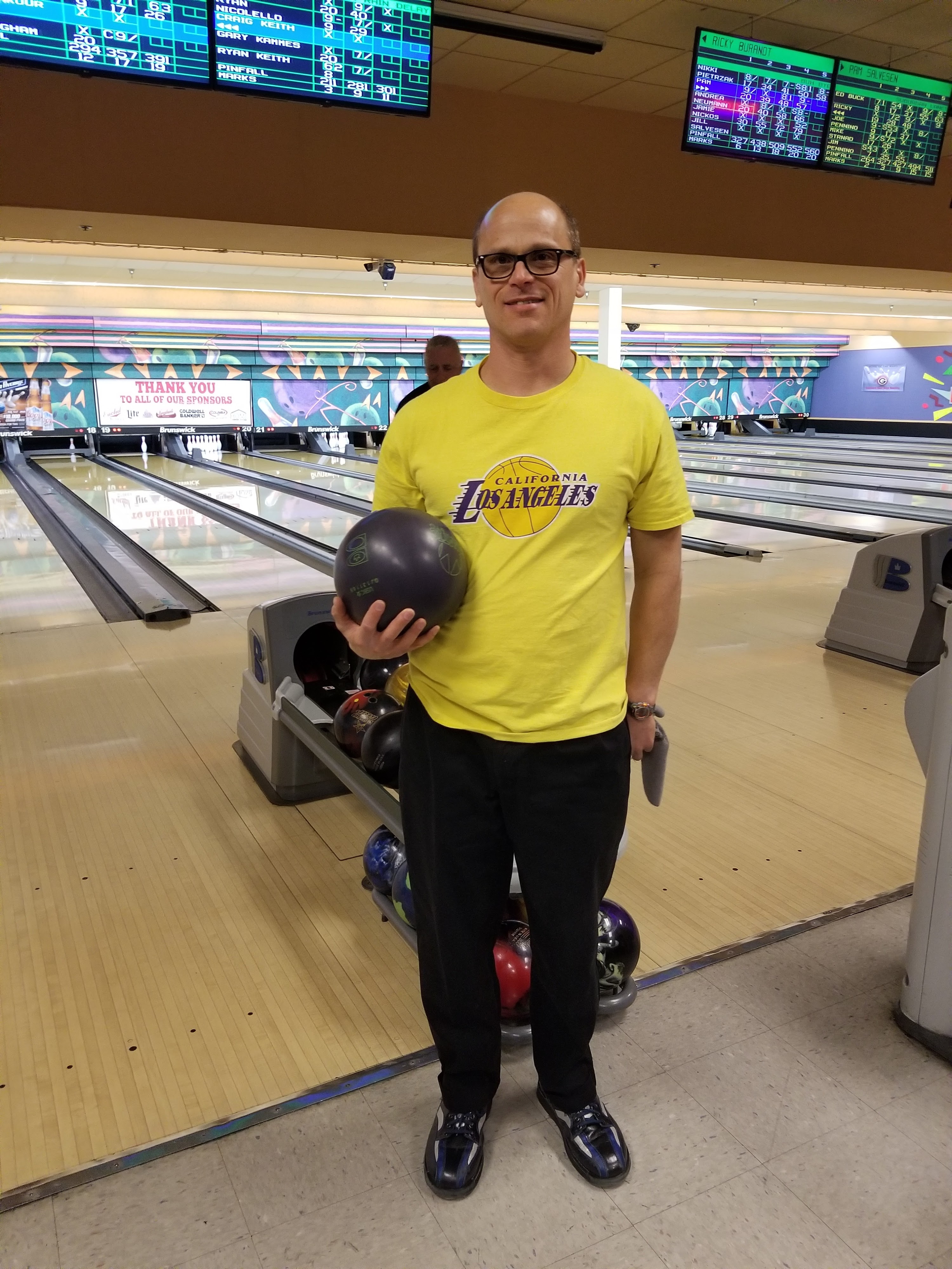 A man in a yellow shirt holding a bowling ball at the start of a bowling lane.