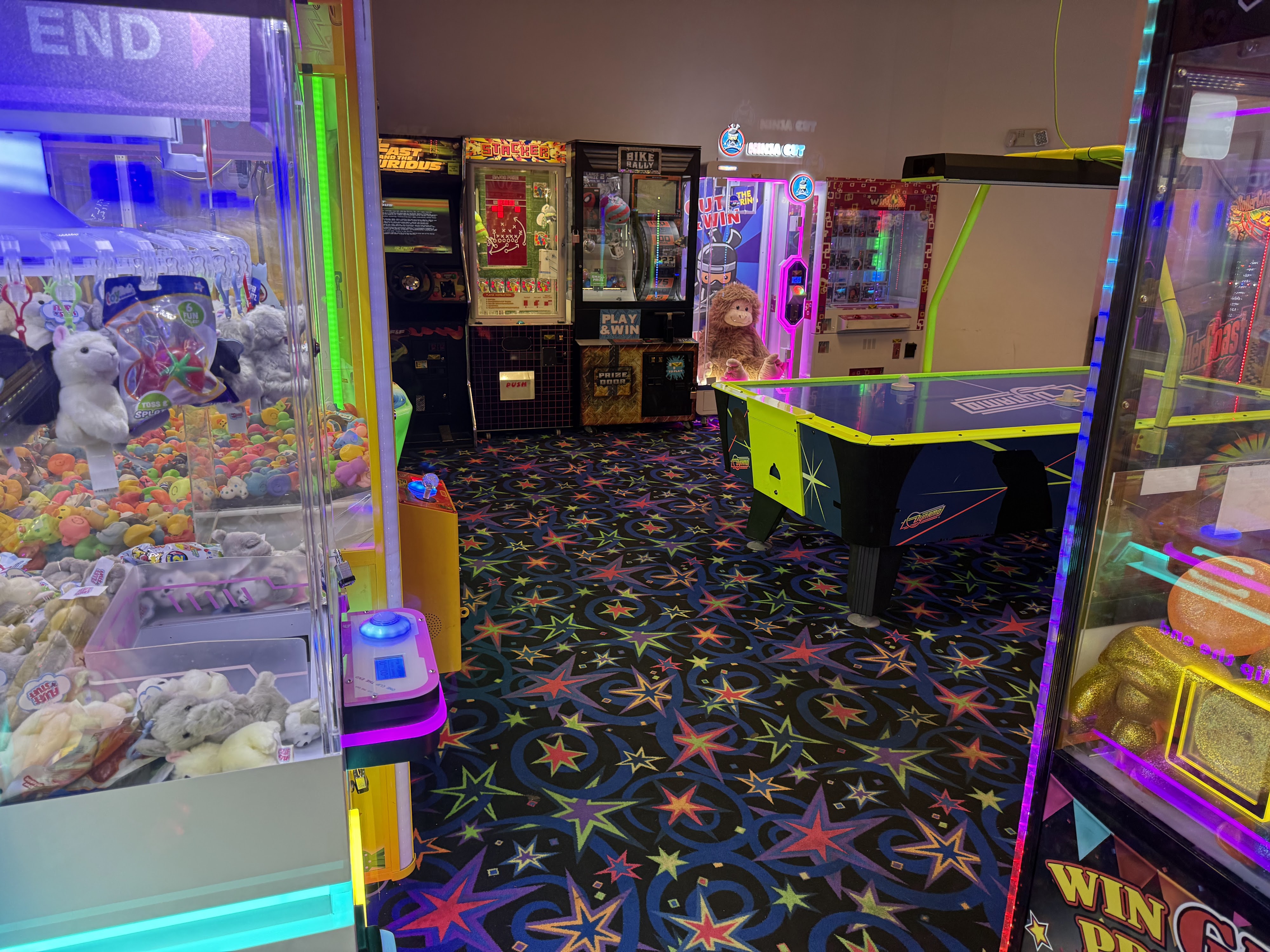 A bowling center arcade featuring claw machines, air hockey, and video games with colorful star-patterned carpeting.