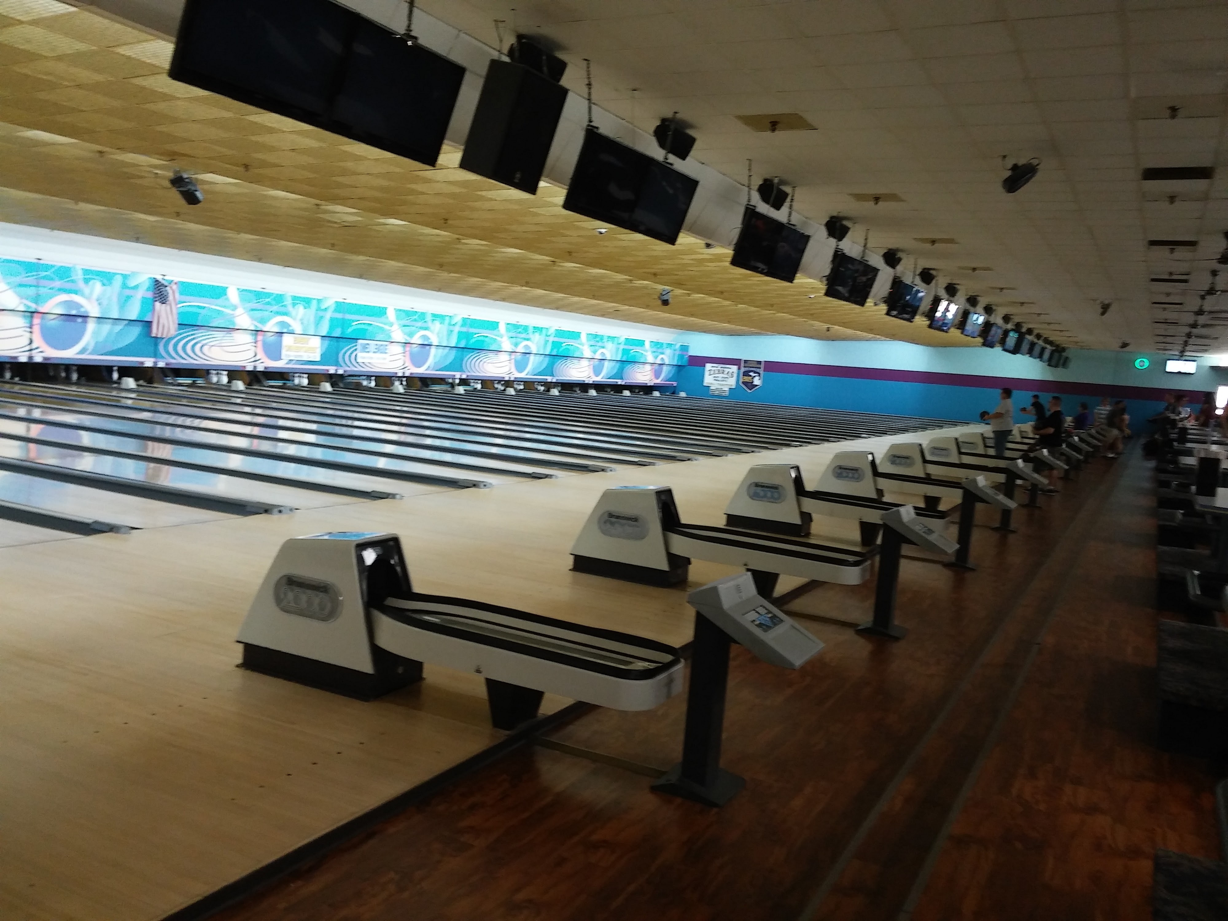 A wide perspective of polished wooden bowling lanes with ball returns and overhead monitors.