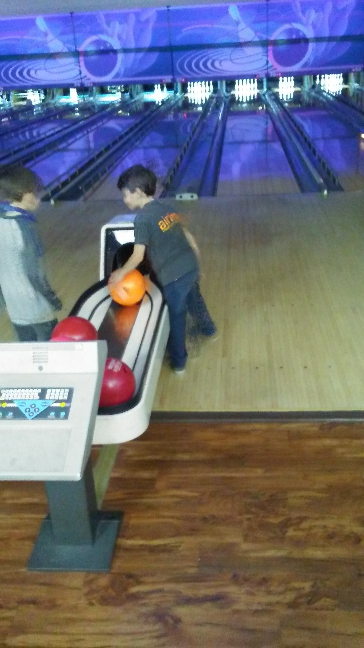 Two young boys selecting bowling balls from a ball return at the bowling alley.