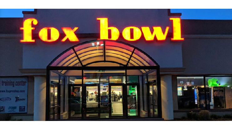 Exterior of Fox Bowl at night with a glowing red and yellow neon sign above the glass entrance.