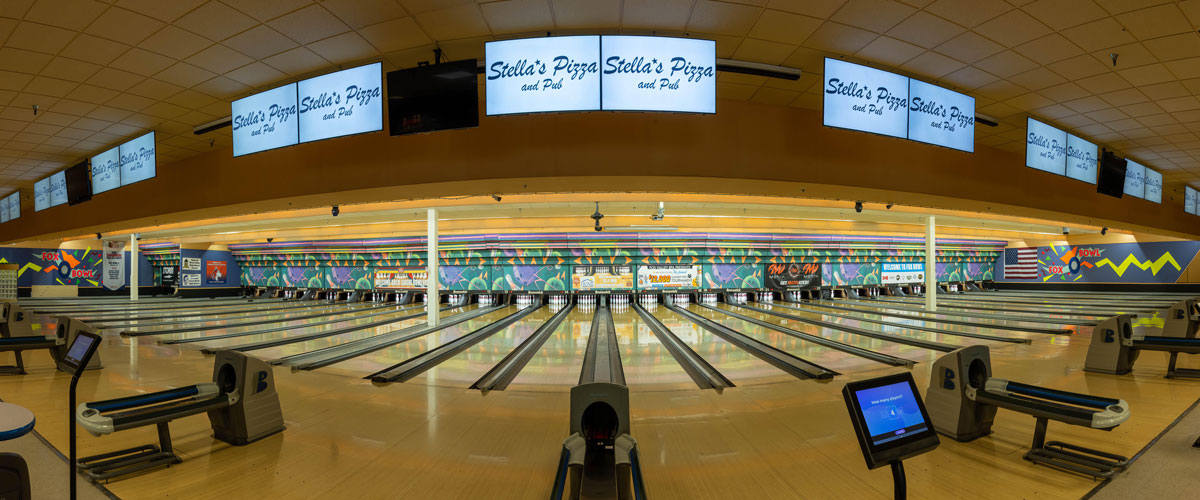 Panoramic view of professional bowling lanes at Fox Bowl with Stella's Pizza and Pub signage on overhead monitors.
