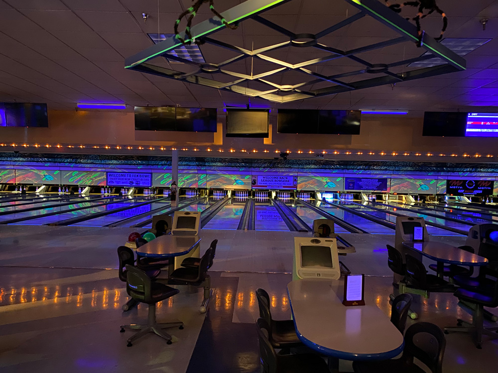 Wide view of bowling lanes at Fox Bowl with glowing blue and purple cosmic lighting and settee seating.