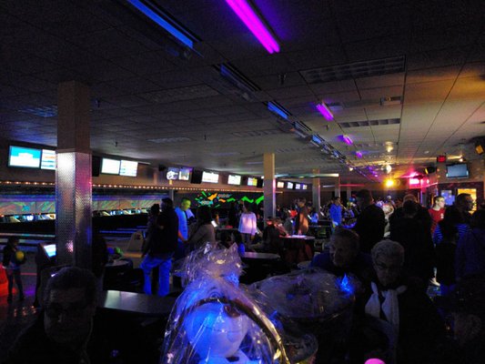 A crowded bowling alley concourse with neon ceiling lights and gift baskets in the foreground.